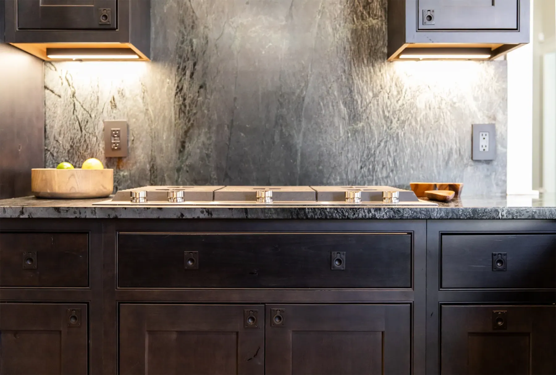 Dark veined stone backsplash and counter behind a cooktop with warm under-cabinet light, Westlake kitchen in Austin, TX