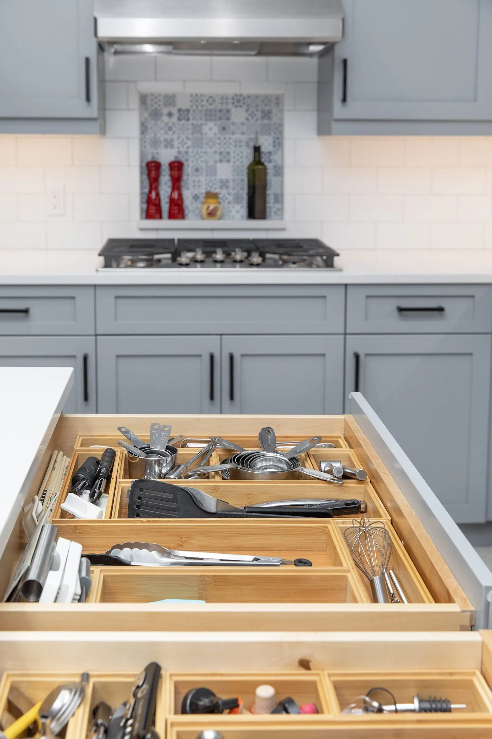 Gray shaker kitchen with open utensil drawers, a gas cooktop and a patterned tile niche, by ATX Renovations