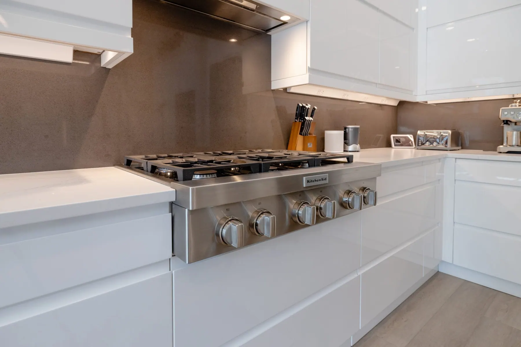Cooktop on a taupe stone backsplash with glossy white handleless cabinets, Bee Cave kitchen