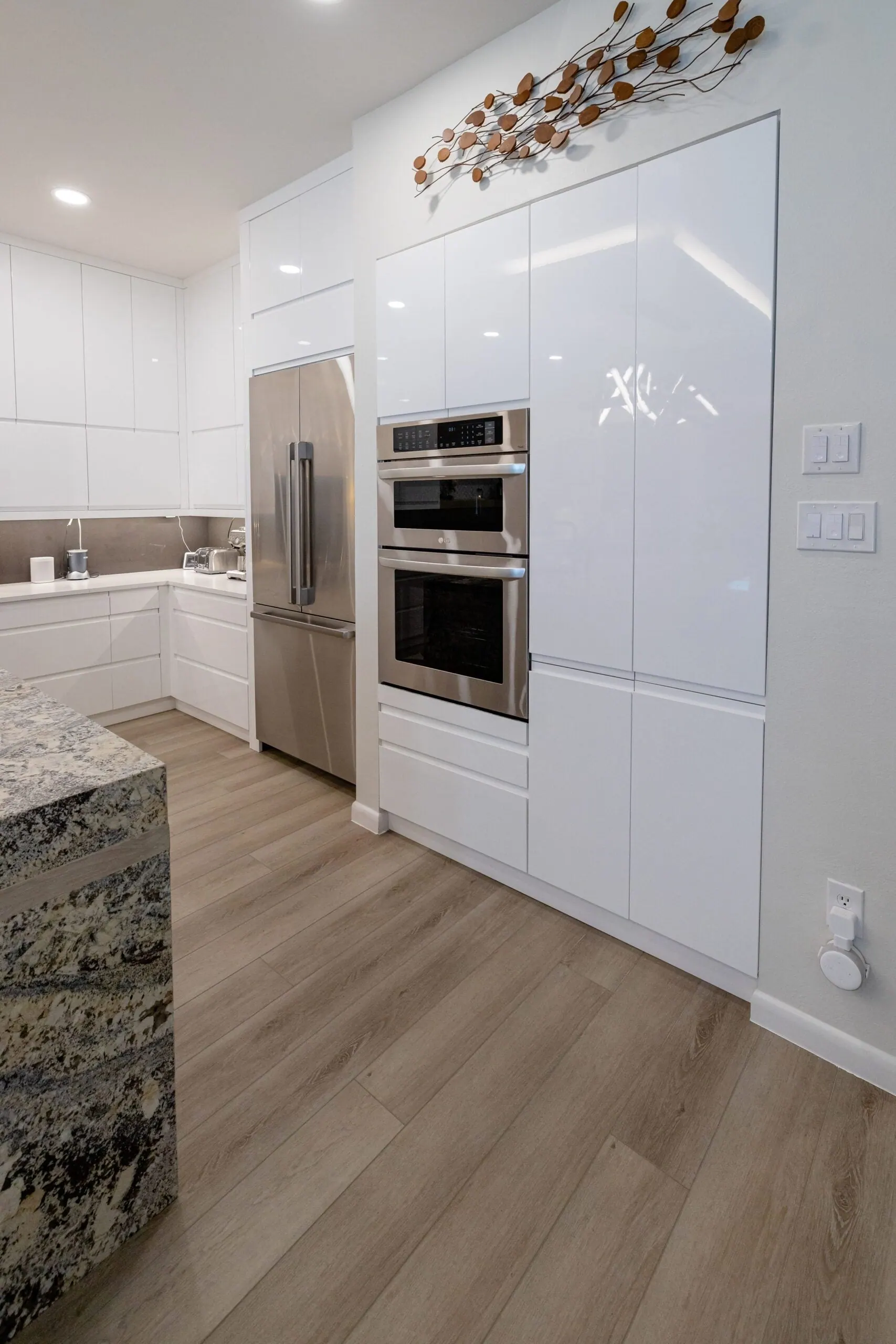 Tall glossy white cabinets with stacked wall ovens and a stainless refrigerator, Bee Cave kitchen