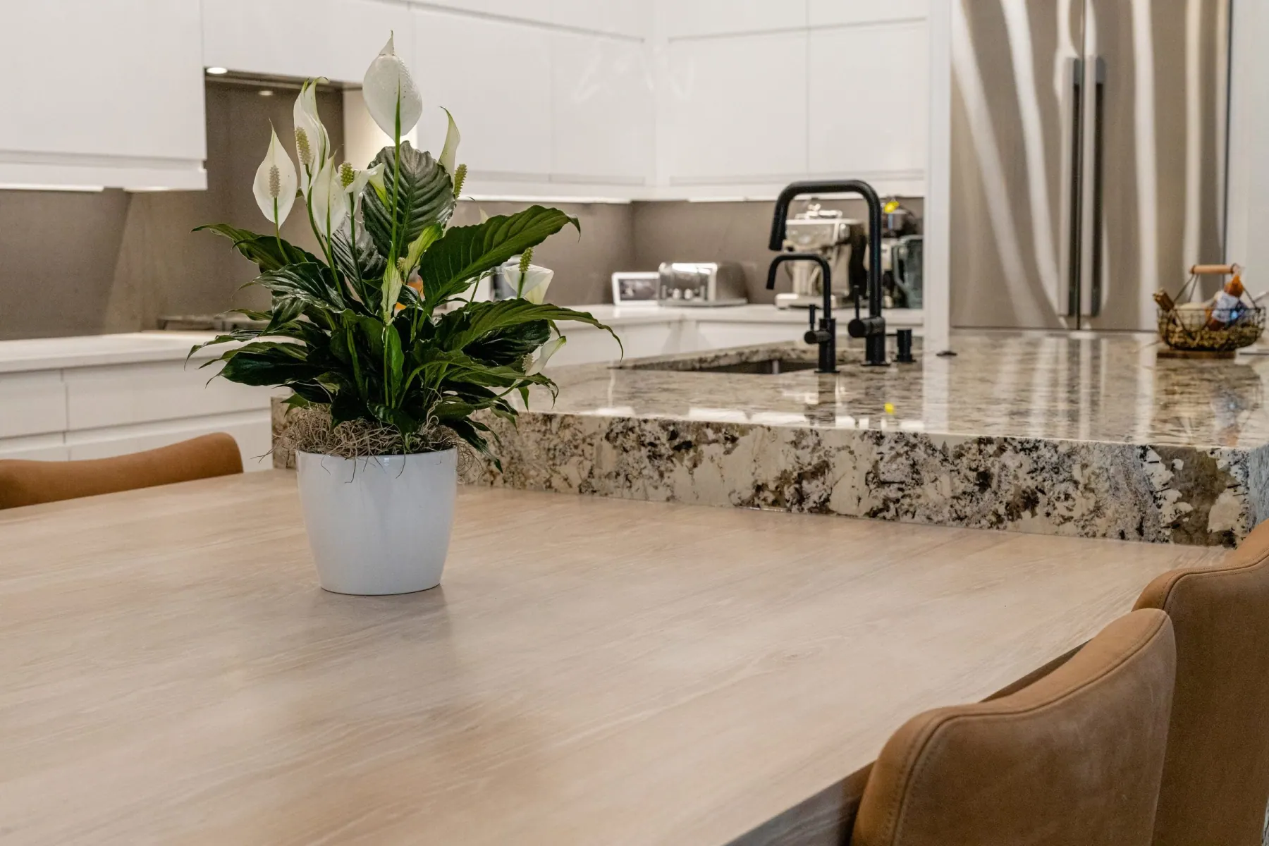 Light wood tabletop beside a granite island with a black faucet and a potted plant, Bee Cave kitchen