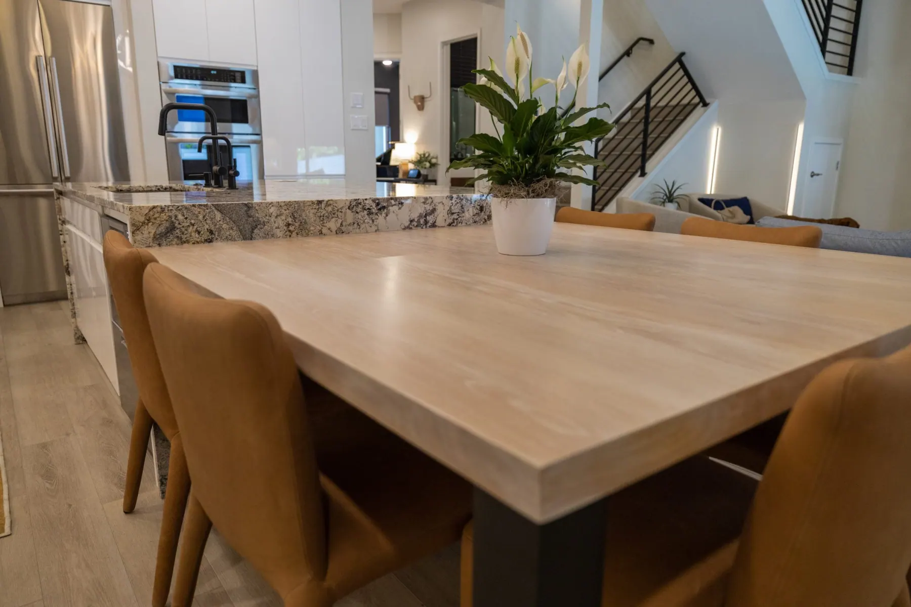 Low view of a light wood table joined to a granite island, with the living room and stairs behind, Bee Cave