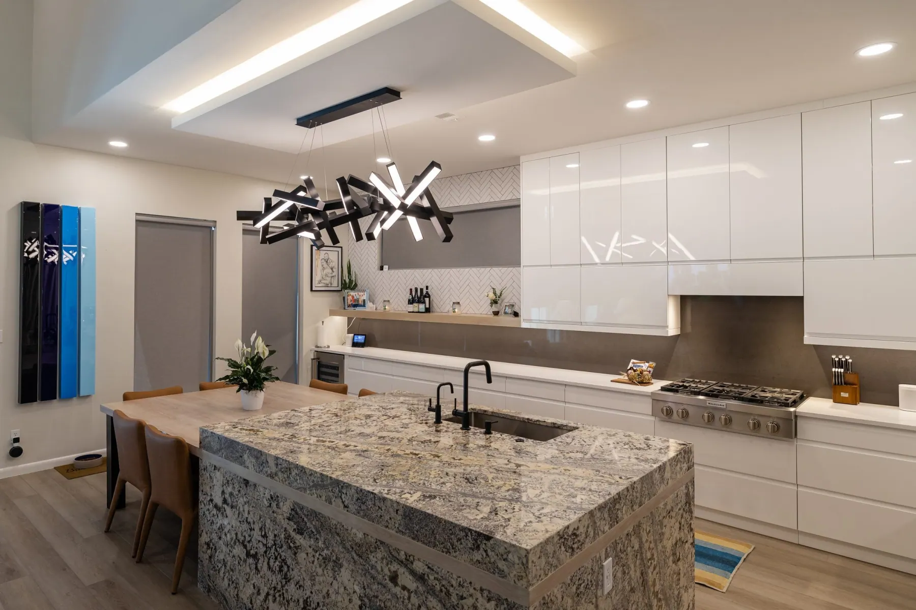 Open kitchen with a granite waterfall island, black linear pendant and glossy white cabinets, Bee Cave, TX