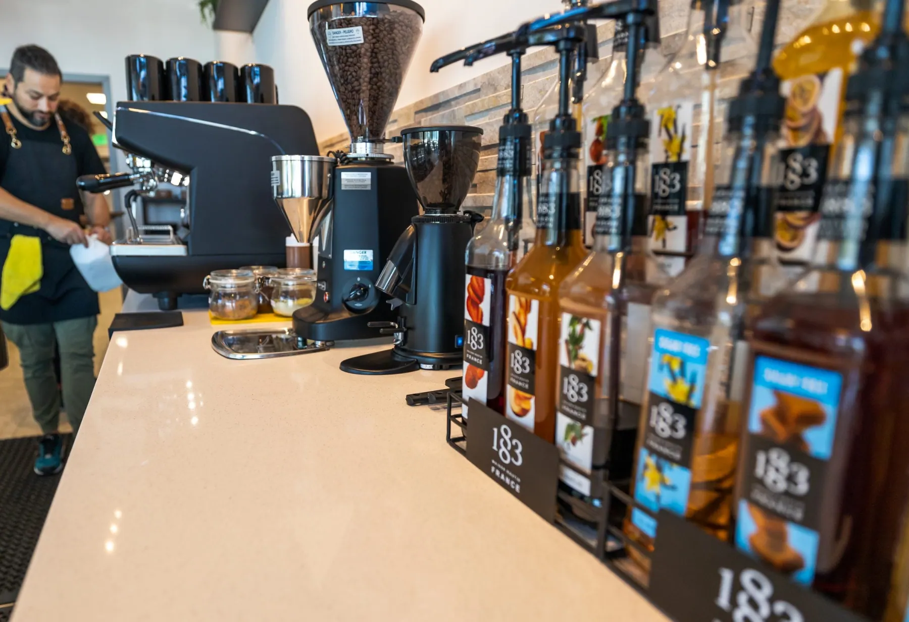 Espresso machine, two grinders and syrup bottles on a quartz cafe counter, commercial cafe project by ATX Renovations