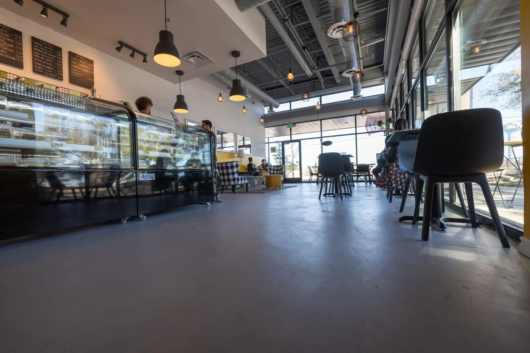 Cafe interior with a glass pastry case, chalkboard menus, black pendant lights and a polished concrete floor