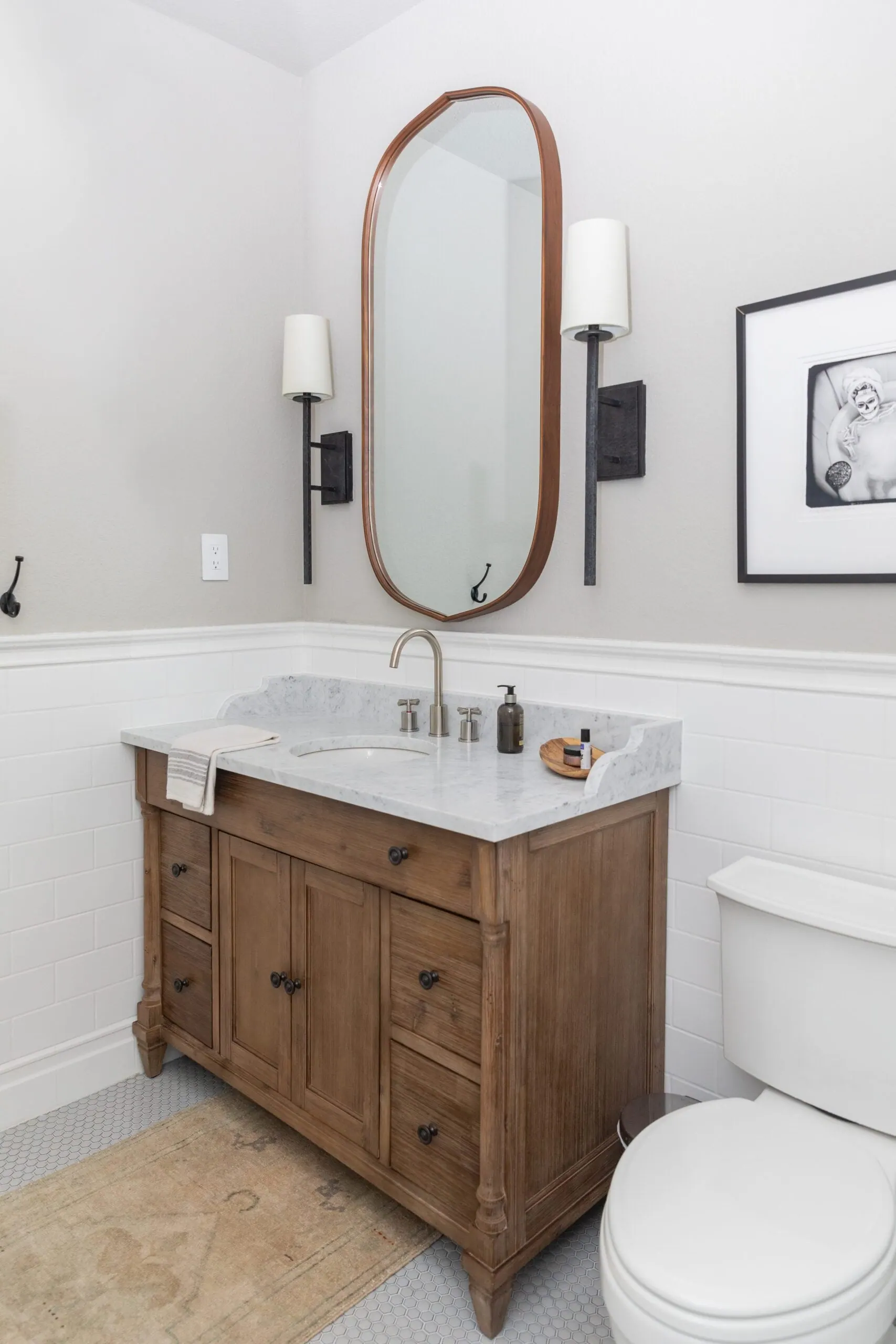 Wood vanity with a marble-look top, oval mirror and wall sconces over white subway tile, Lakeway bathroom