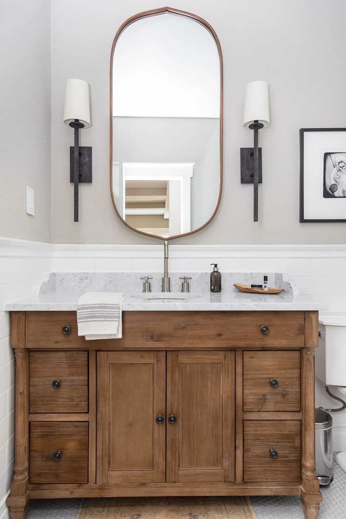 Wood vanity with marble-look top, oval mirror and black sconces, bathroom remodeled by ATX Renovations in Lakeway