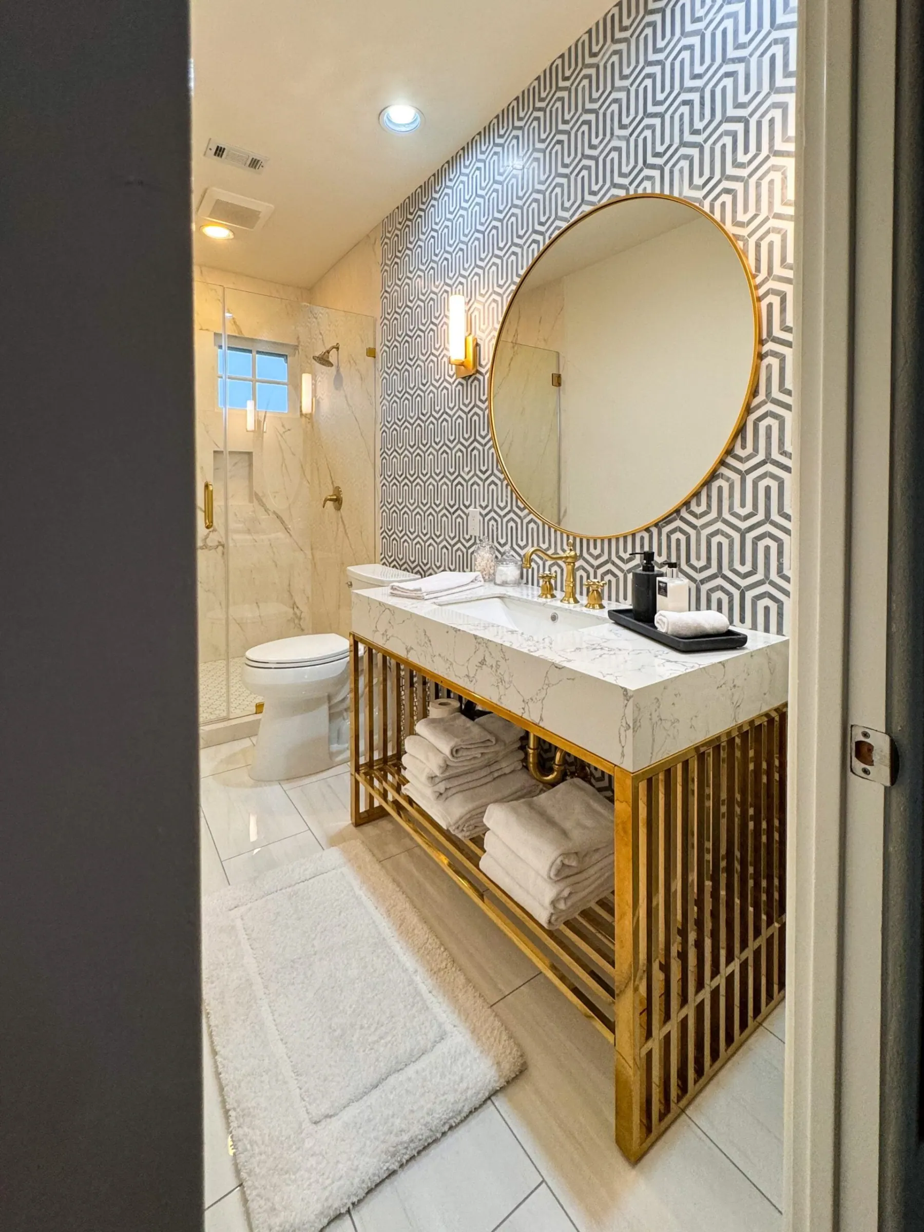 Bathroom with a gold vanity, geometric tile wall and frameless glass shower, remodeled in Lakeway, TX