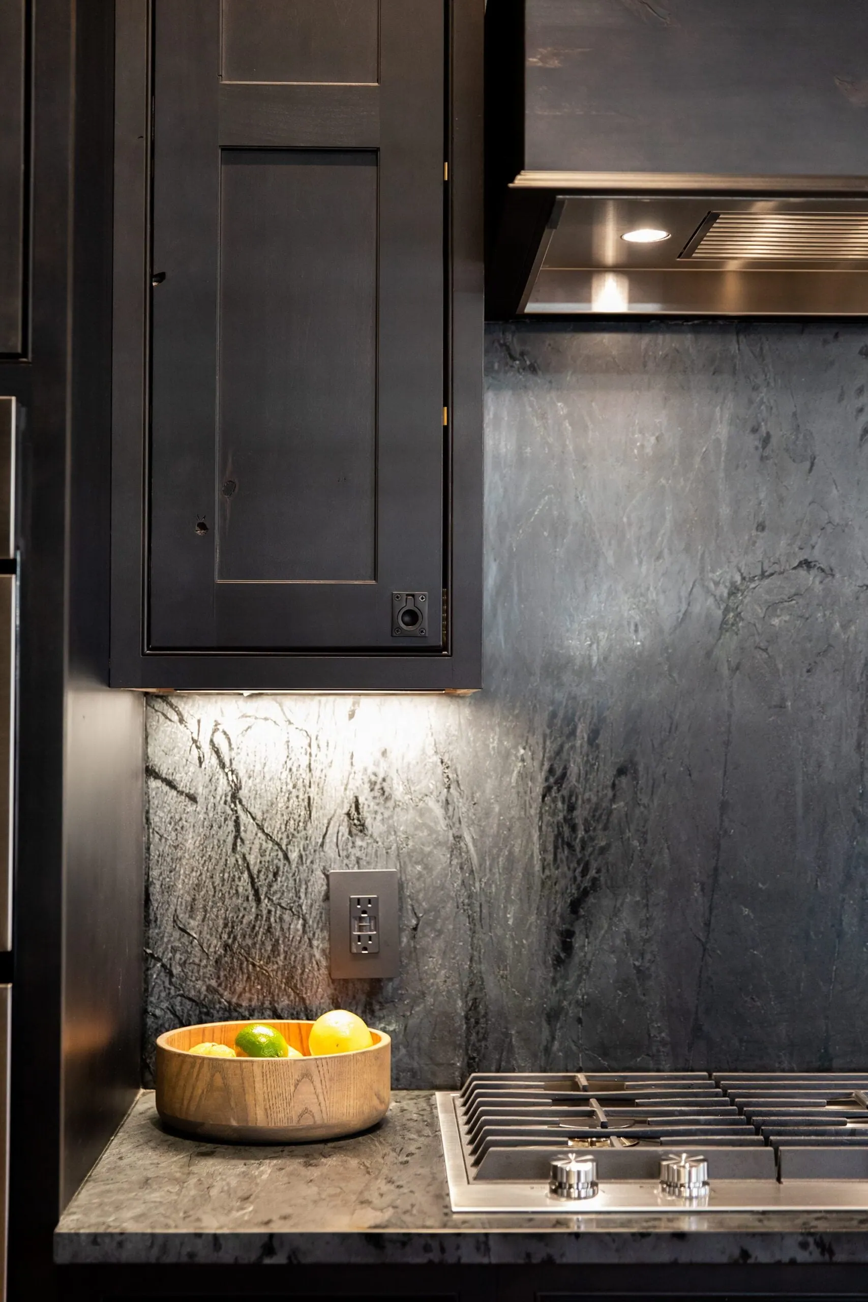 Dark veined stone backsplash and counter next to a stained cabinet, with a wooden bowl of limes, Westlake kitchen